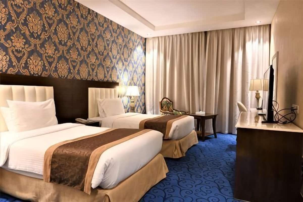 Habitación de hotel con dos camas, un escritorio, una silla y un ventanal con cortinas.