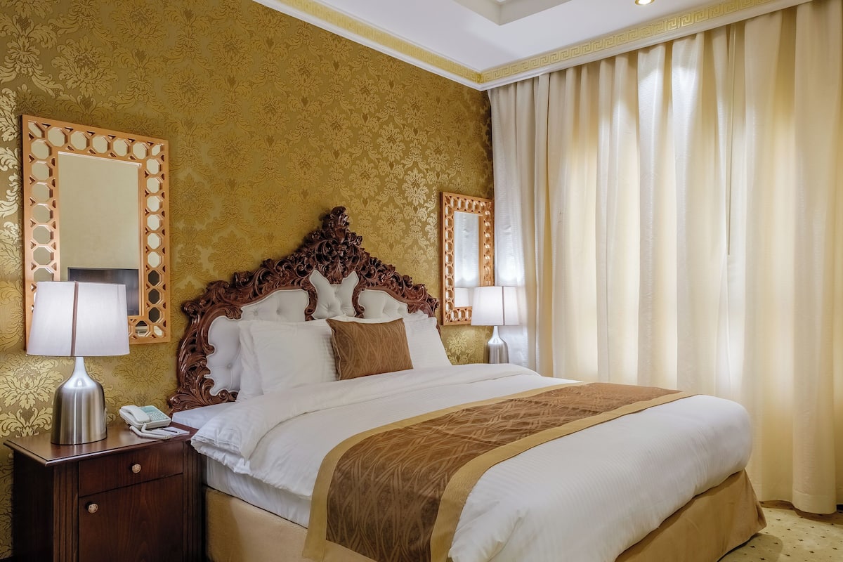 Habitación de hotel con una cama grande, dos mesitas de noche con lámparas, un teléfono y un espejo decorativo.