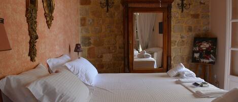 Quarto de hotel com uma cama grande, parede de pedra, candelabro e um quadro na parede.