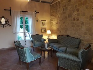 A cozy living room with a stone wall, a window with curtains, and a lamp. - Alekos Beach Houses - Natura Rossa (Kefalonia)