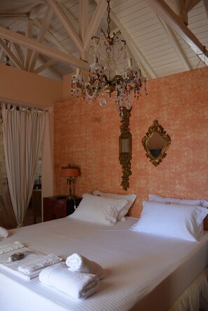 Een hotelkamer met een groot bed, een kroonluchter, een spiegel en een raam met gordijnen.