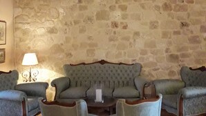 A room with a stone wall, a chandelier, a sofa set, and a table with a candle. - Alekos Beach Houses - Natura Rossa (Kefalonia)