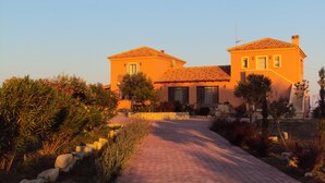 A two-story building with a tiled roof and a paved pathway leading to the entrance. - Alekos Beach Houses - Natura Rossa (Kefalonia)