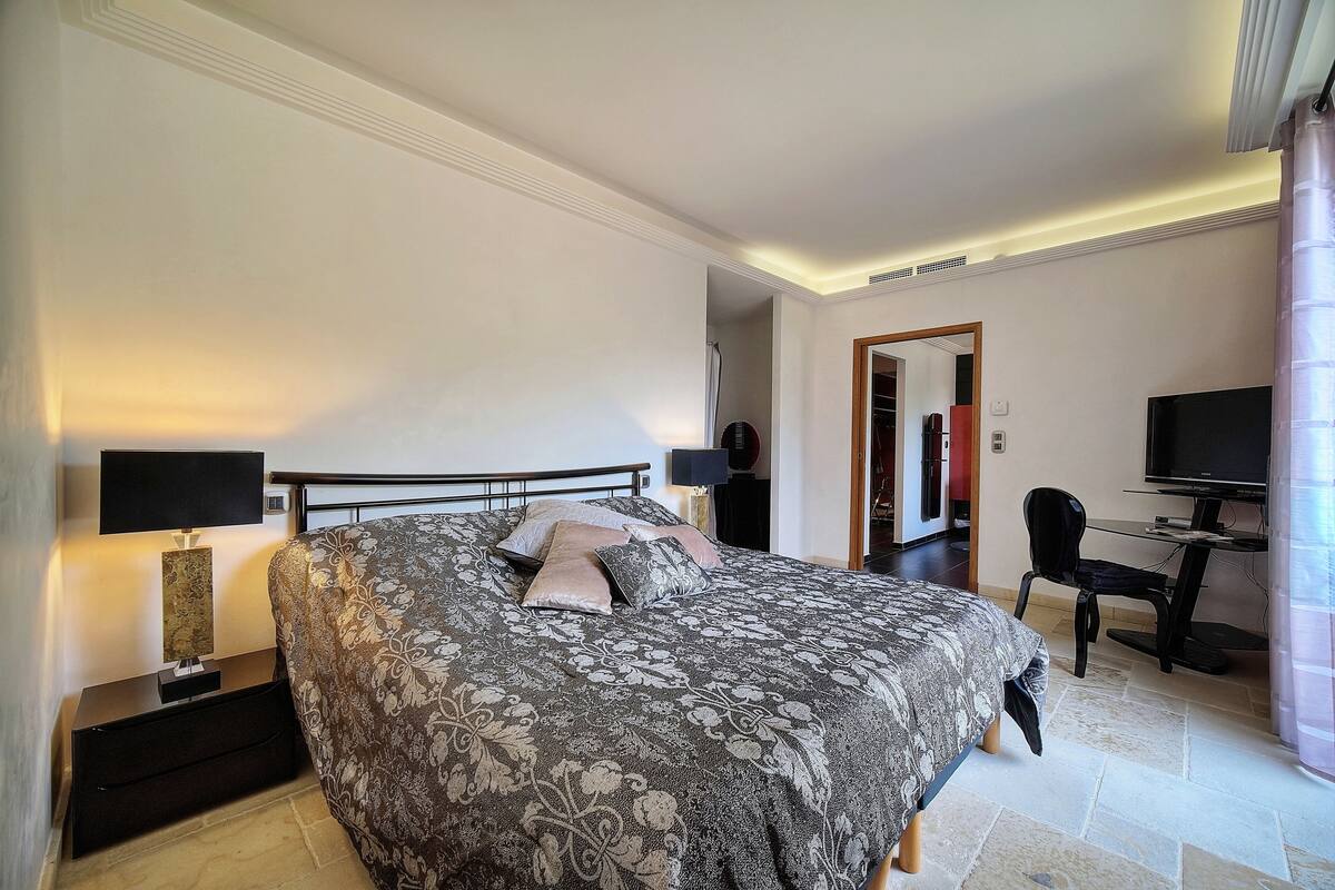 A bedroom with a bed, bedside tables, a desk, a chair, a television, and a mirror.