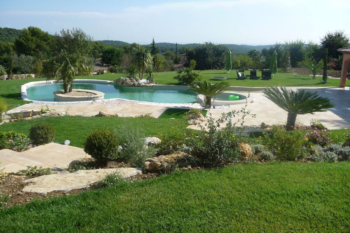 A landscaped backyard with a swimming pool, palm trees, and a patio area.