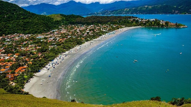A coastal town with a long sandy beach, clear blue waters, and lush green hills in the background. - PRIS Hotel (São Sebastião)