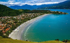 A coastal town with a long sandy beach, clear blue waters, and lush green hills in the background. - PRIS Hotel (São Sebastião)