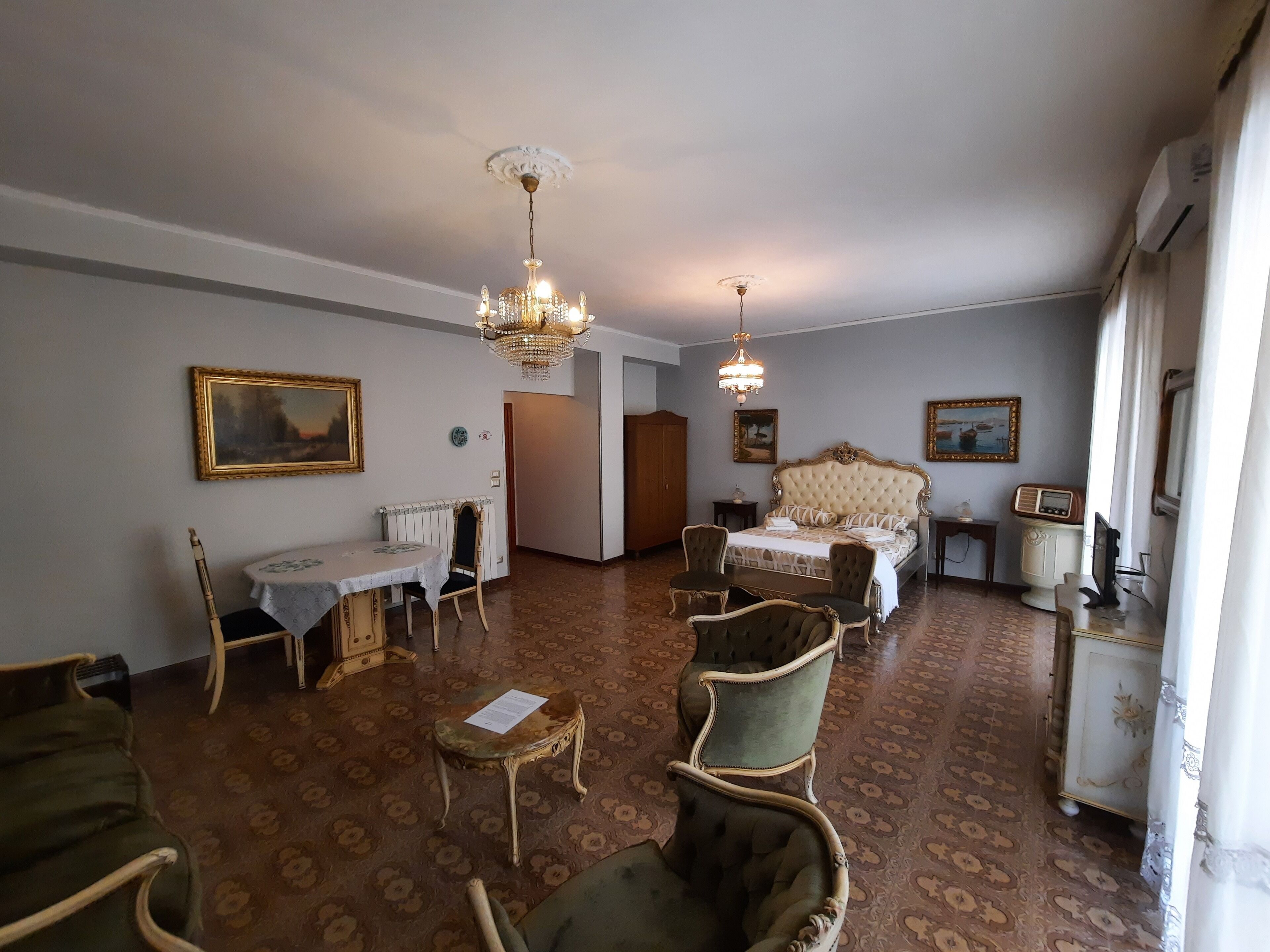 Una stanza con un letto grande, un tavolo da pranzo con sedie, un lampadario e un termosifone.