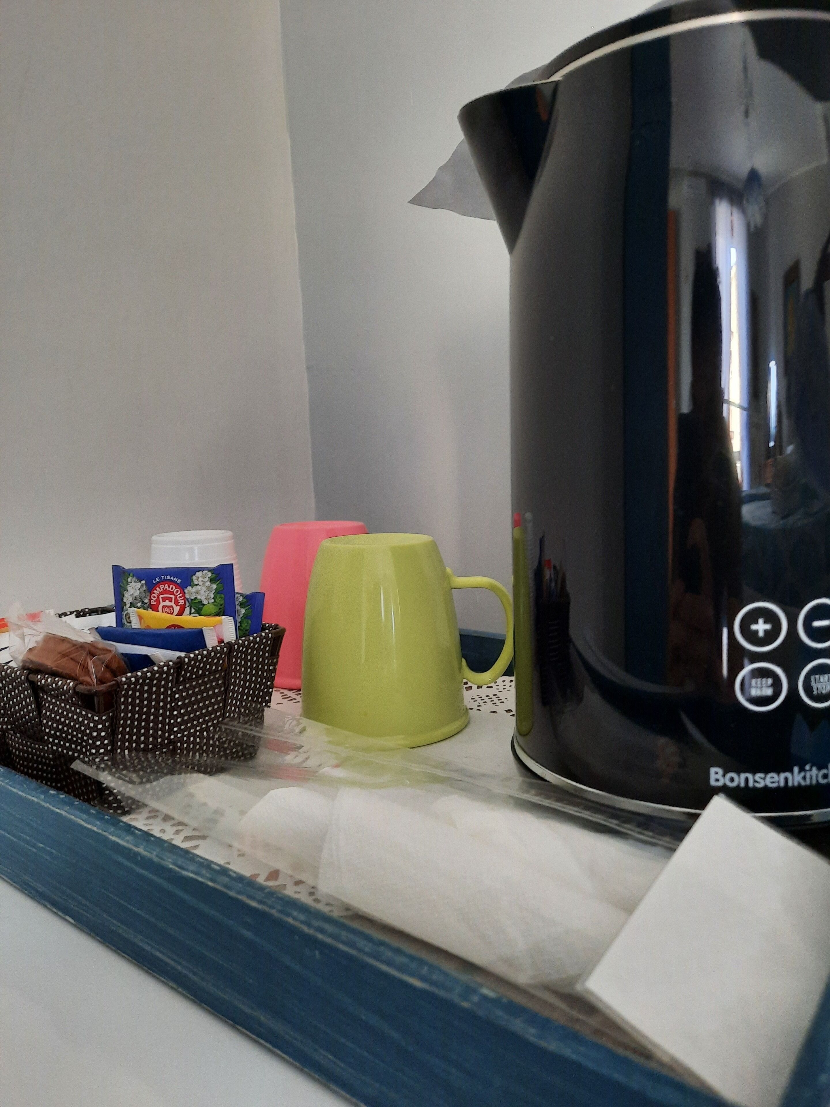Eine Küchenarbeitsplatte mit einer schwarzen Kaffeemaschine, einer grünen Tasse, einer gepunkteten Tasche und verpackten Lebensmitteln.