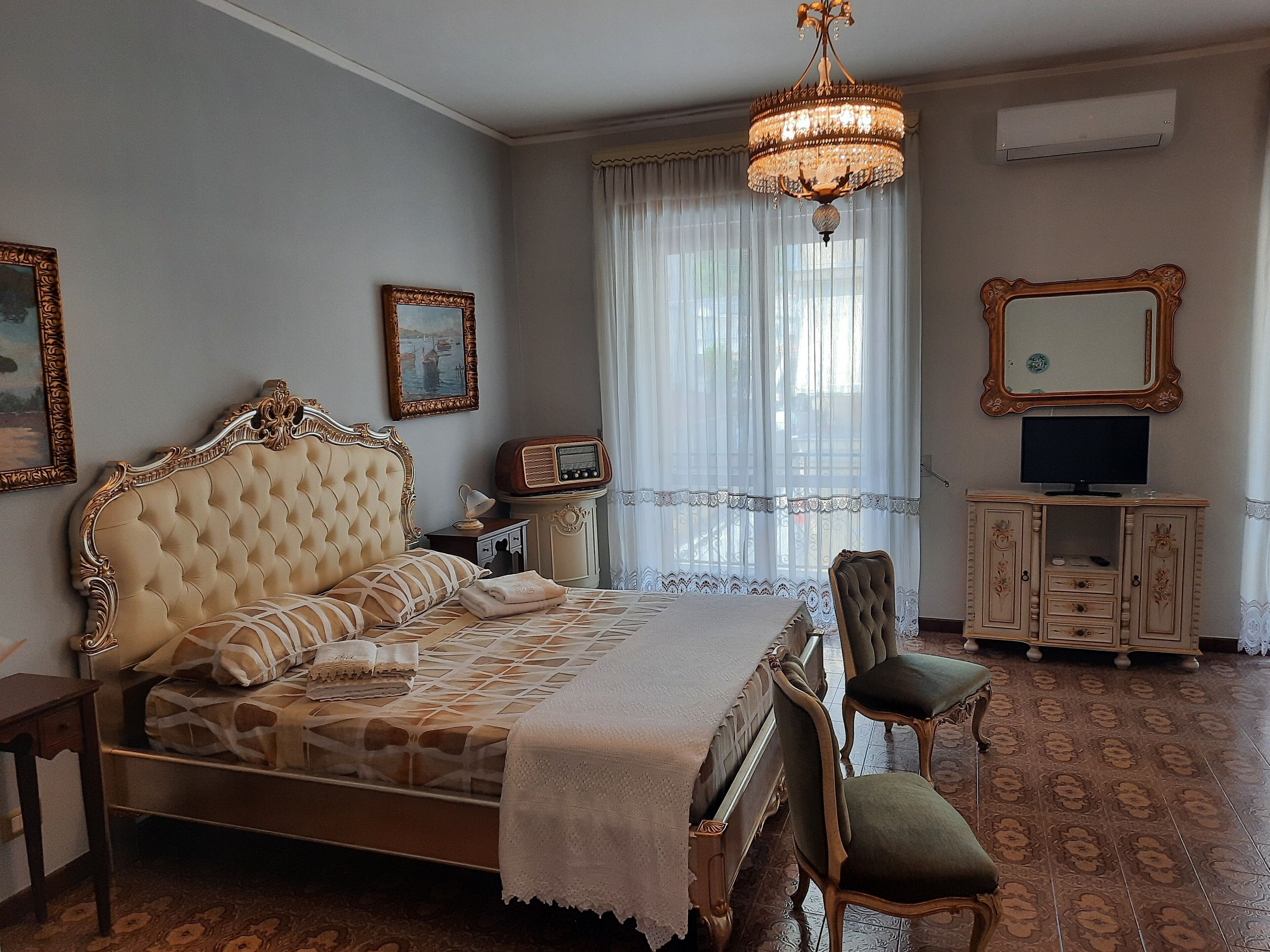 A classic bedroom with a large bed, a vanity with a mirror, a television, and a chandelier.