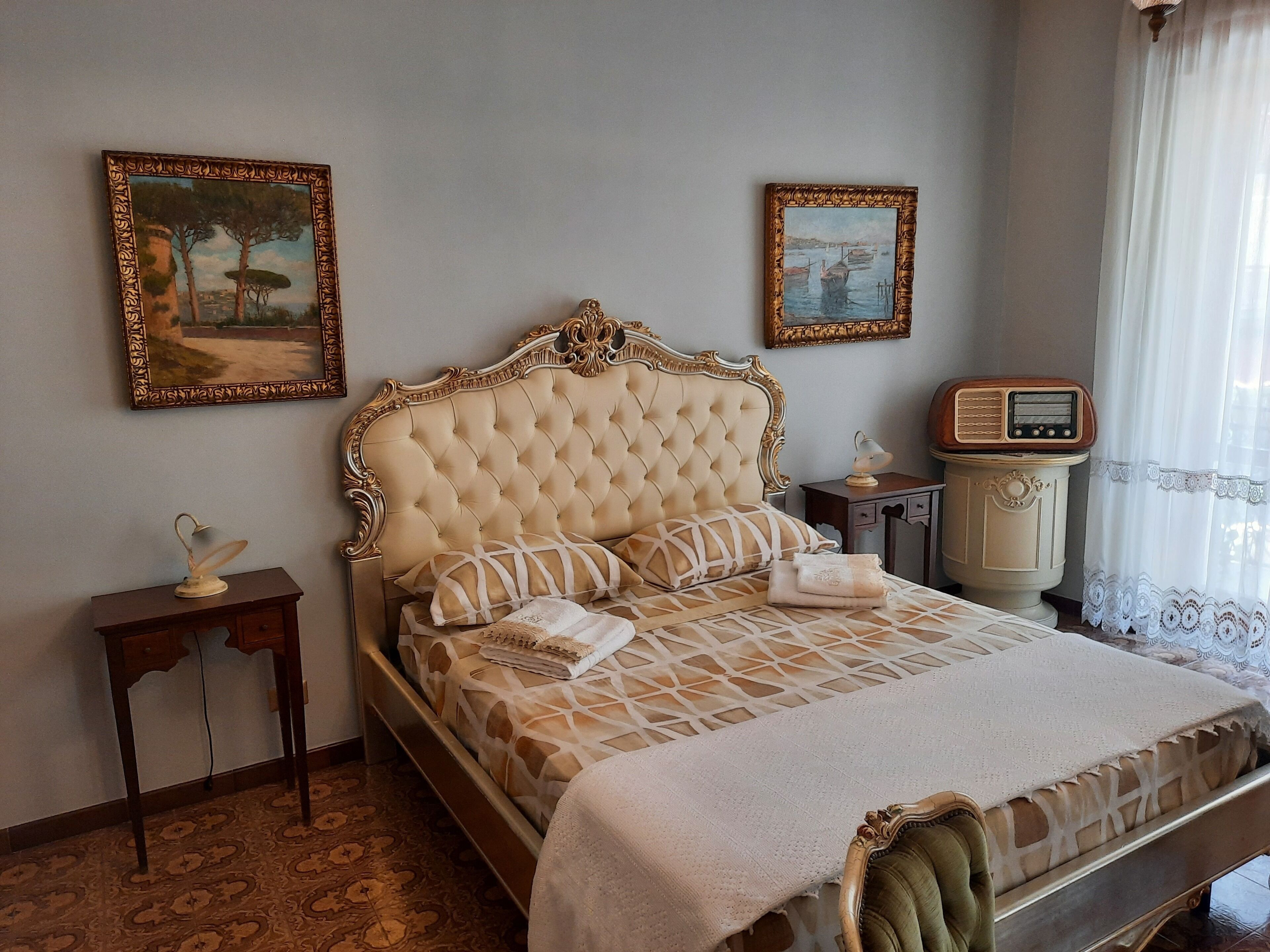 Una camera da letto con testiera capitonata, un letto con biancheria a motivi decorativi, un comodino con una lampada e una radio.