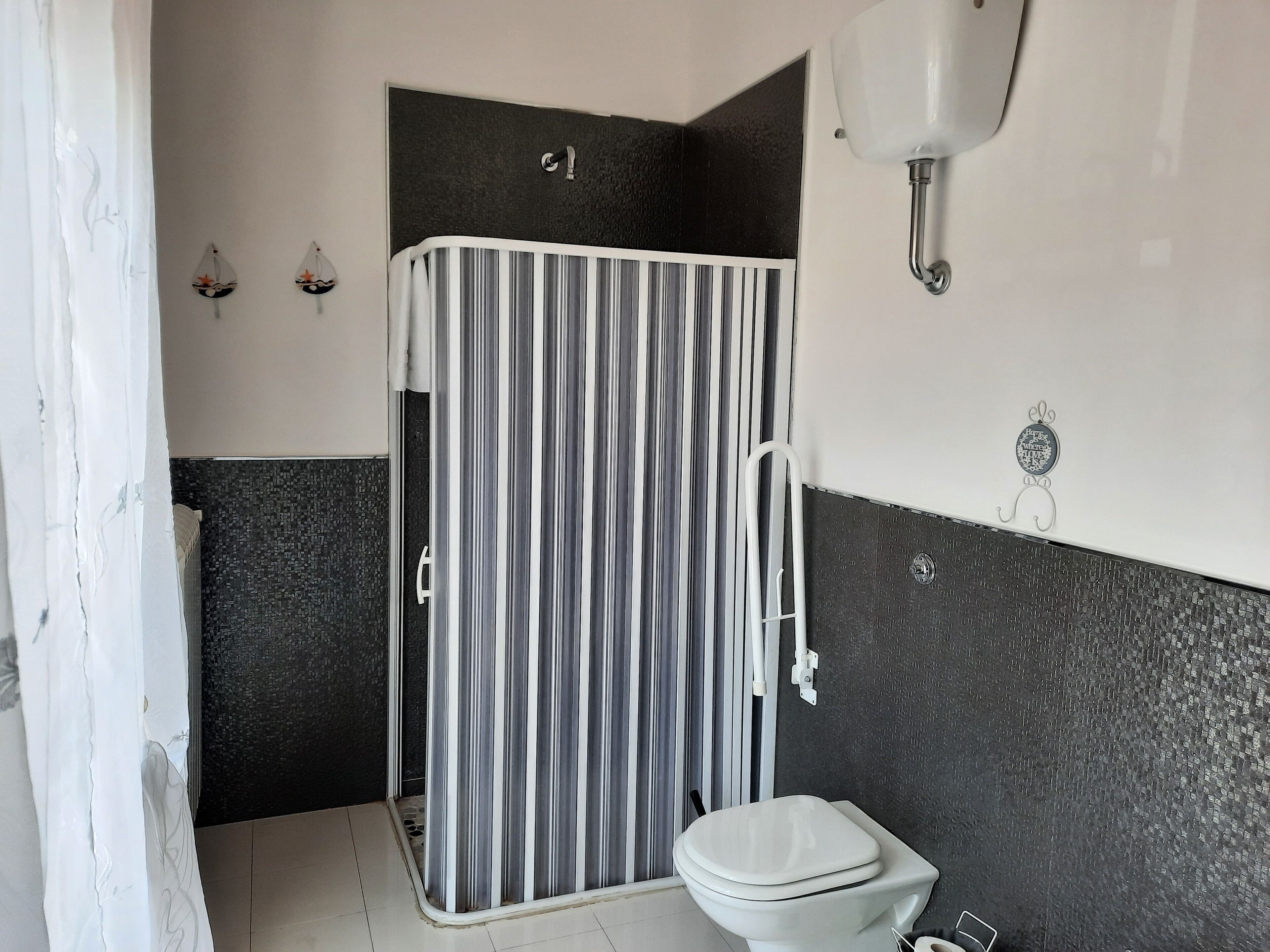 Un bagno con tenda da doccia a righe, un water e un lavandino fissato al muro.