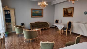Ein Zimmer mit einem gemusterten Teppich, einem grünen Sofa, einem Esstisch mit Stühlen, einer Chandelüster und einem Bücherregal.
