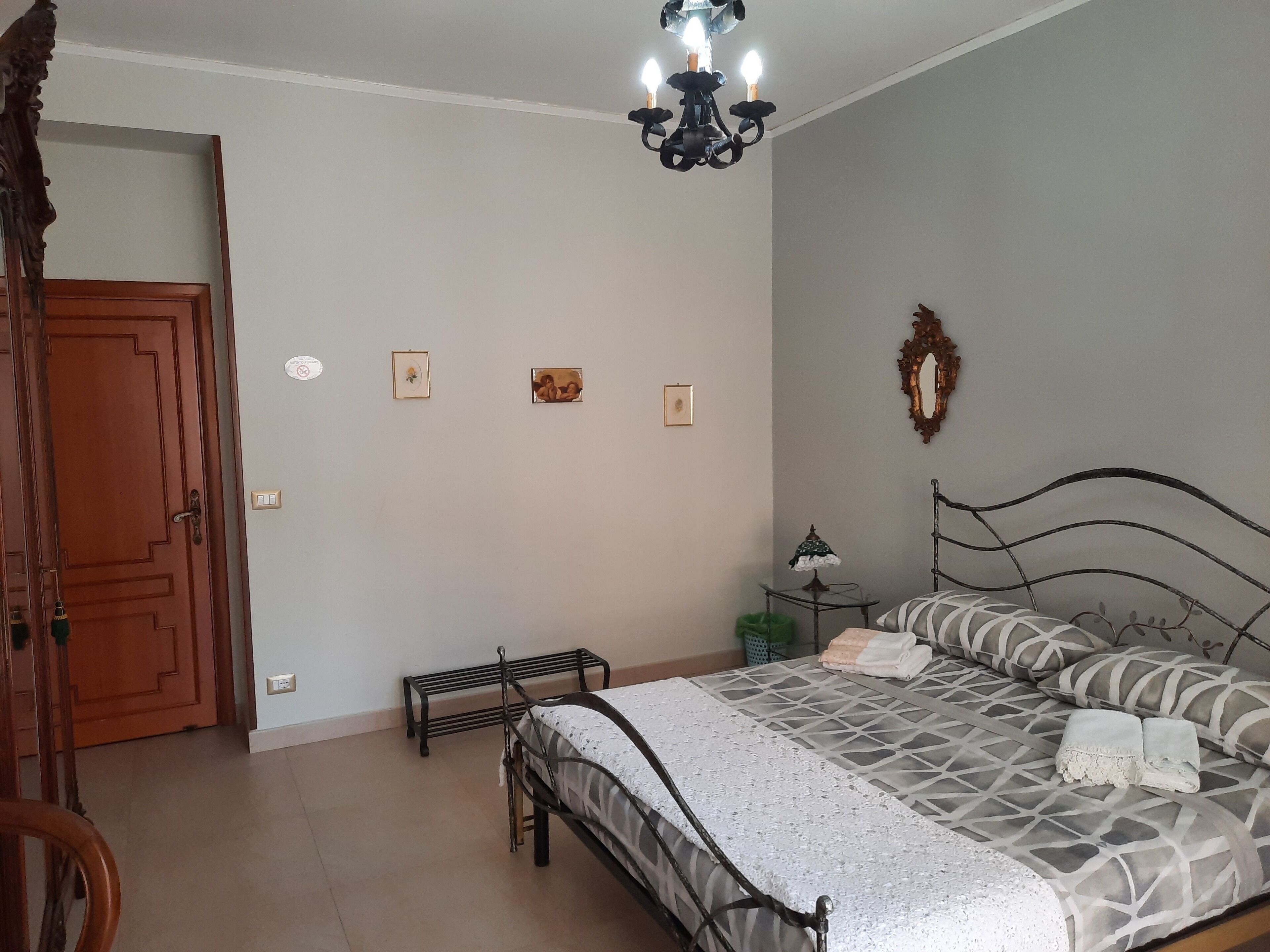 A bedroom with a bed, a wooden door, a small table with a lamp, and a mirror on the wall.