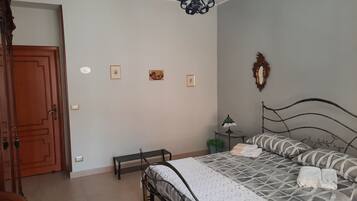 A bedroom with a bed, a wooden door, a small table with a lamp, and a mirror on the wall.