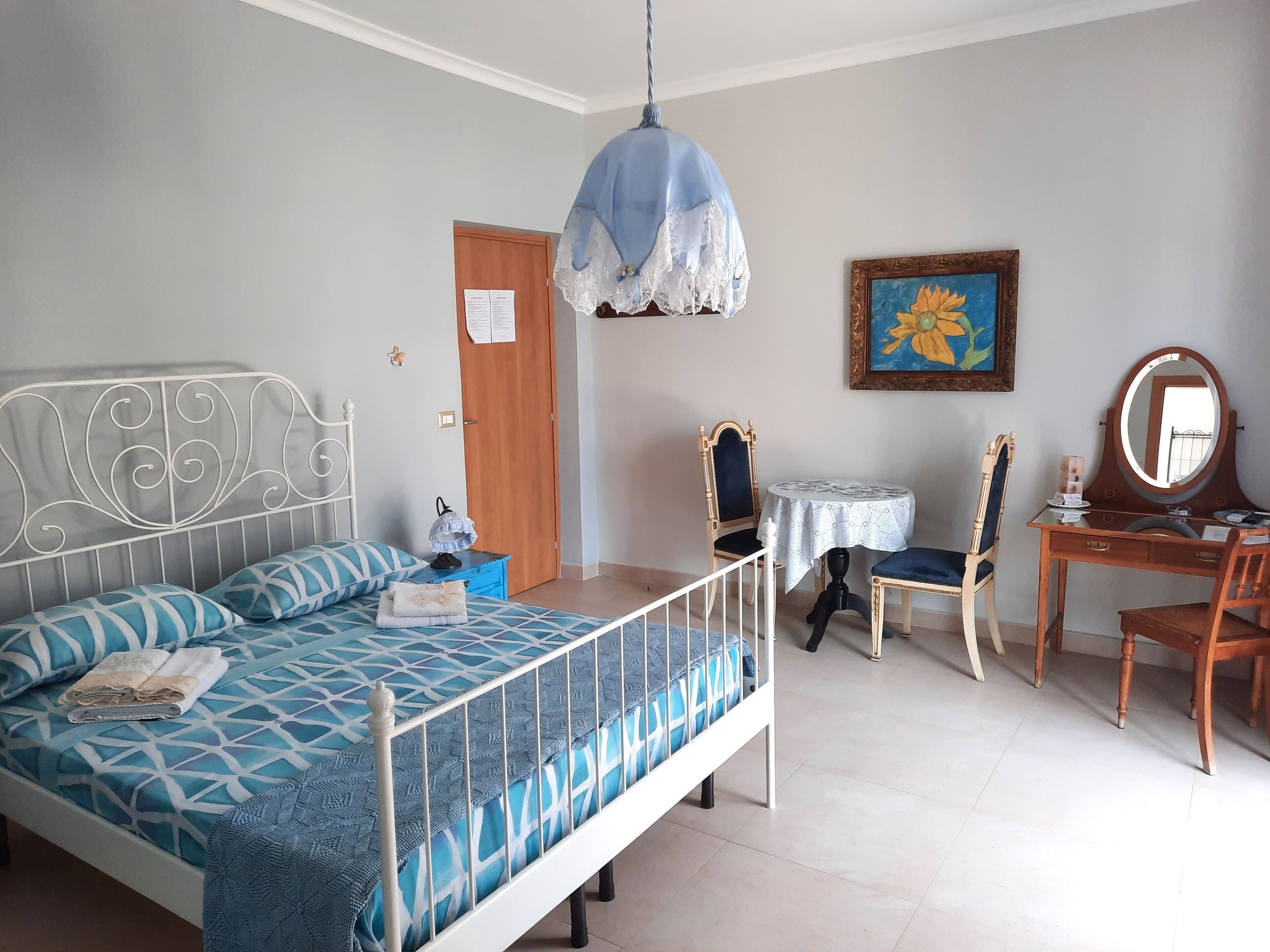 A bedroom with a bed, a desk, a chair, a small table, and a hanging light fixture.