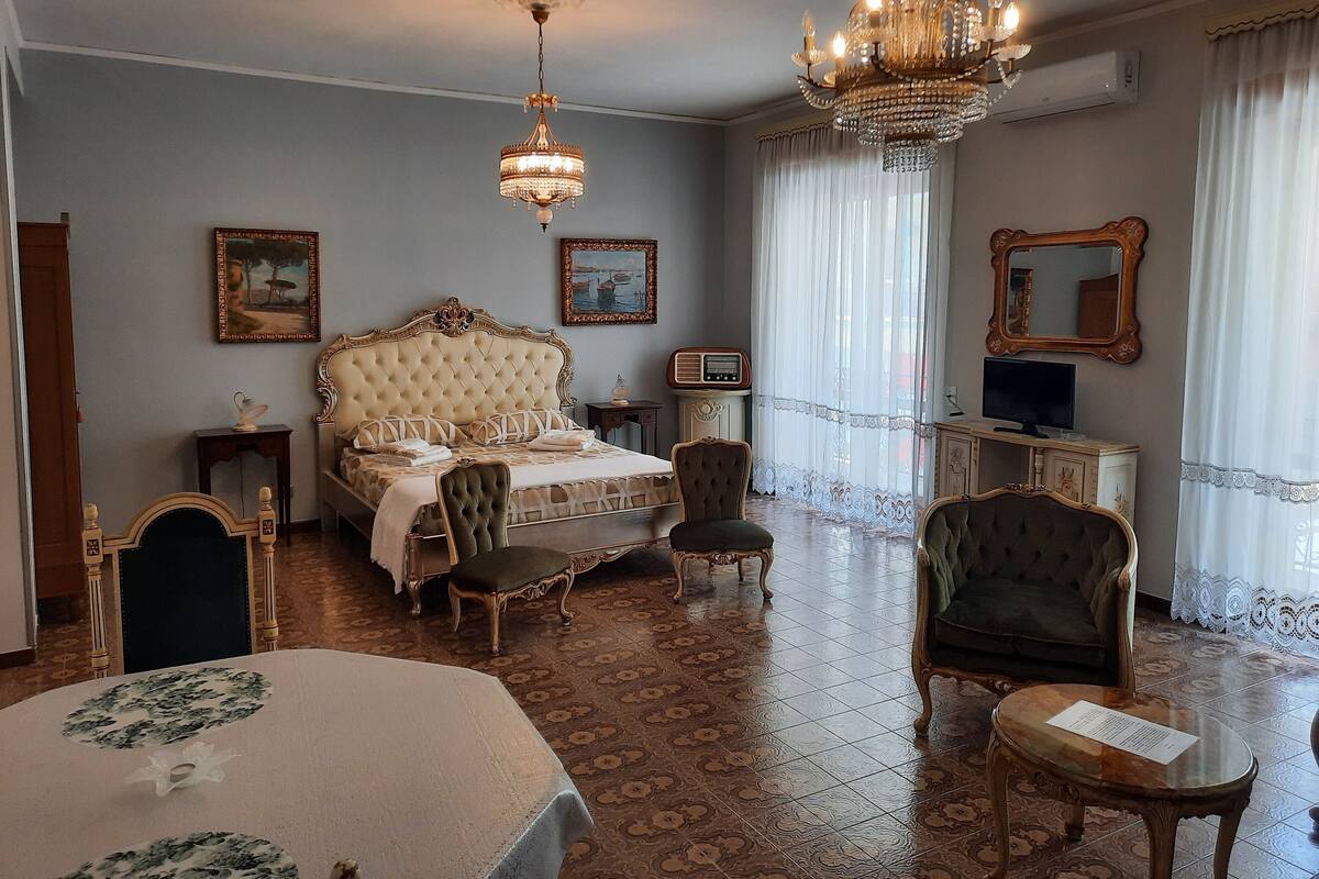 A spacious room with a large bed, two chairs, a small table, and a television.