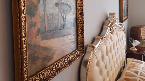 A bedroom with a large ornate picture frame on the wall, a tufted headboard, and a small bedside table with a lamp. - Villa Ada B&B (Agropoli)