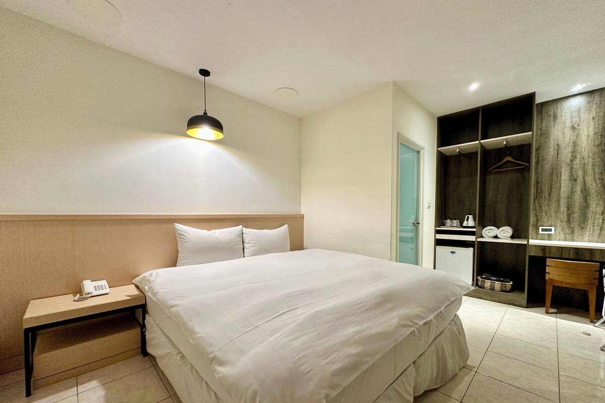 A hotel room with a large bed, bedside table, and a wardrobe.