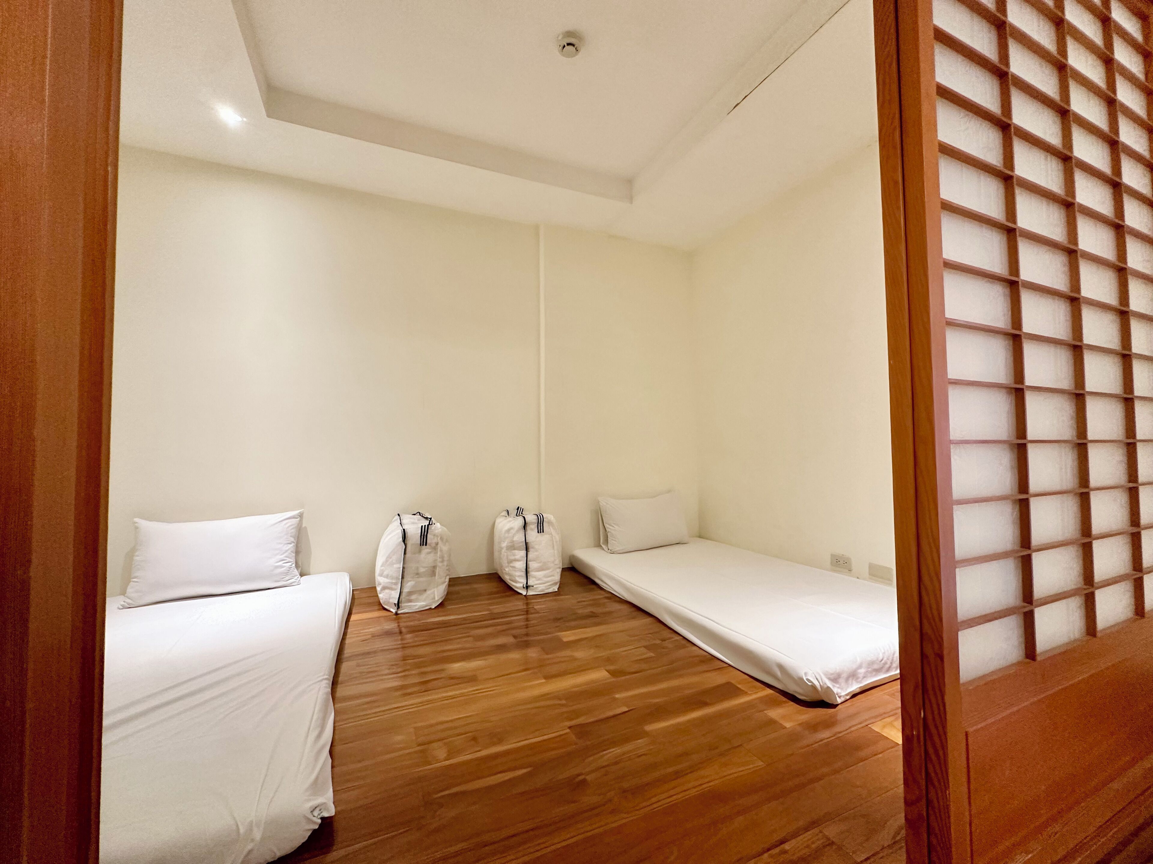Una habitación con dos camas individuales, piso de madera y una puerta corredera con diseño de cuadrícula.