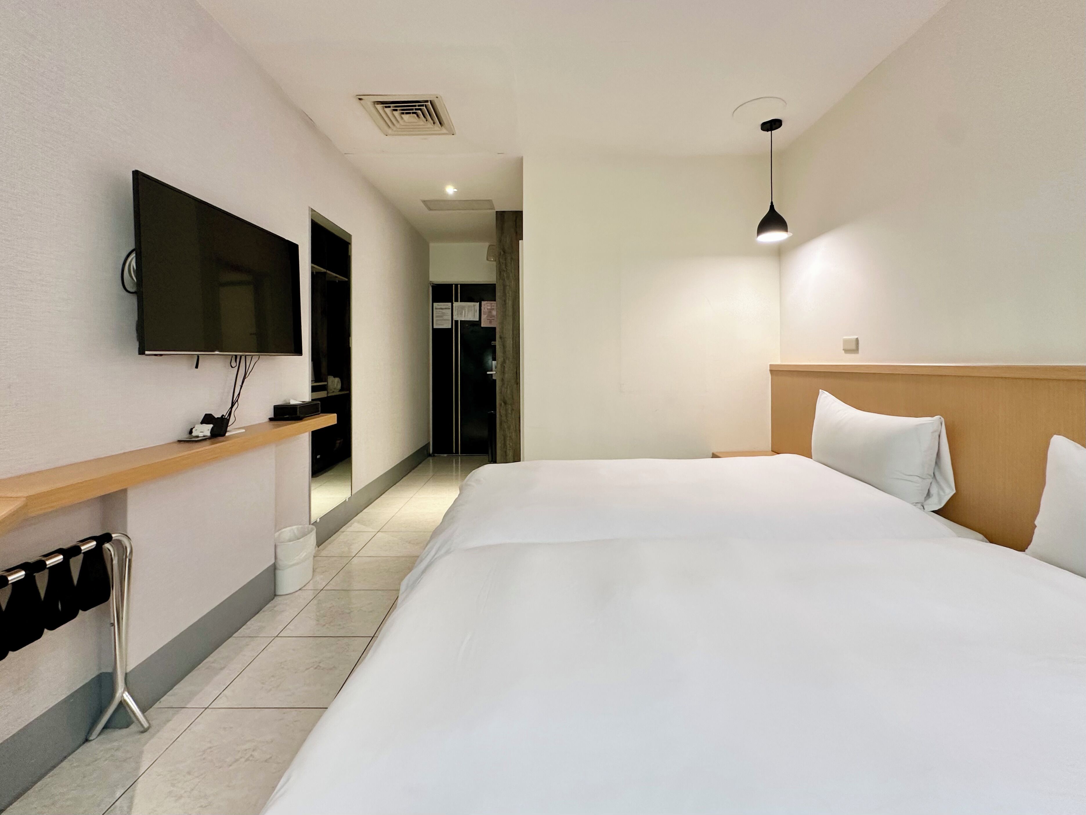 Habitación de hotel con una cama grande, un televisor montado en la pared, un cabecero de madera y un escritorio pequeño con un espejo.