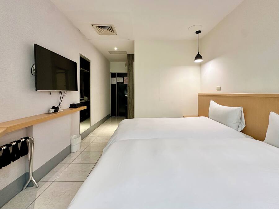 Habitación de hotel con una cama grande, un televisor montado en la pared, un cabecero de madera y un escritorio pequeño con un espejo.