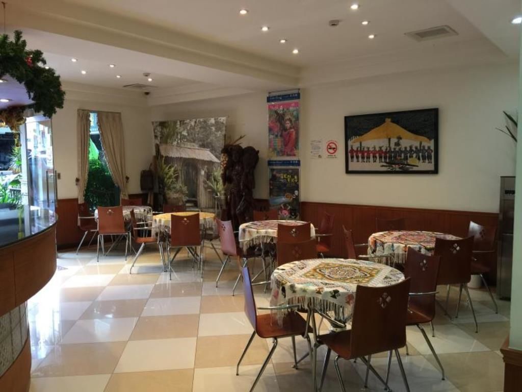 A dining area with multiple round tables and chairs, a large painting on the wall, and a view of the outdoors through a glass door.