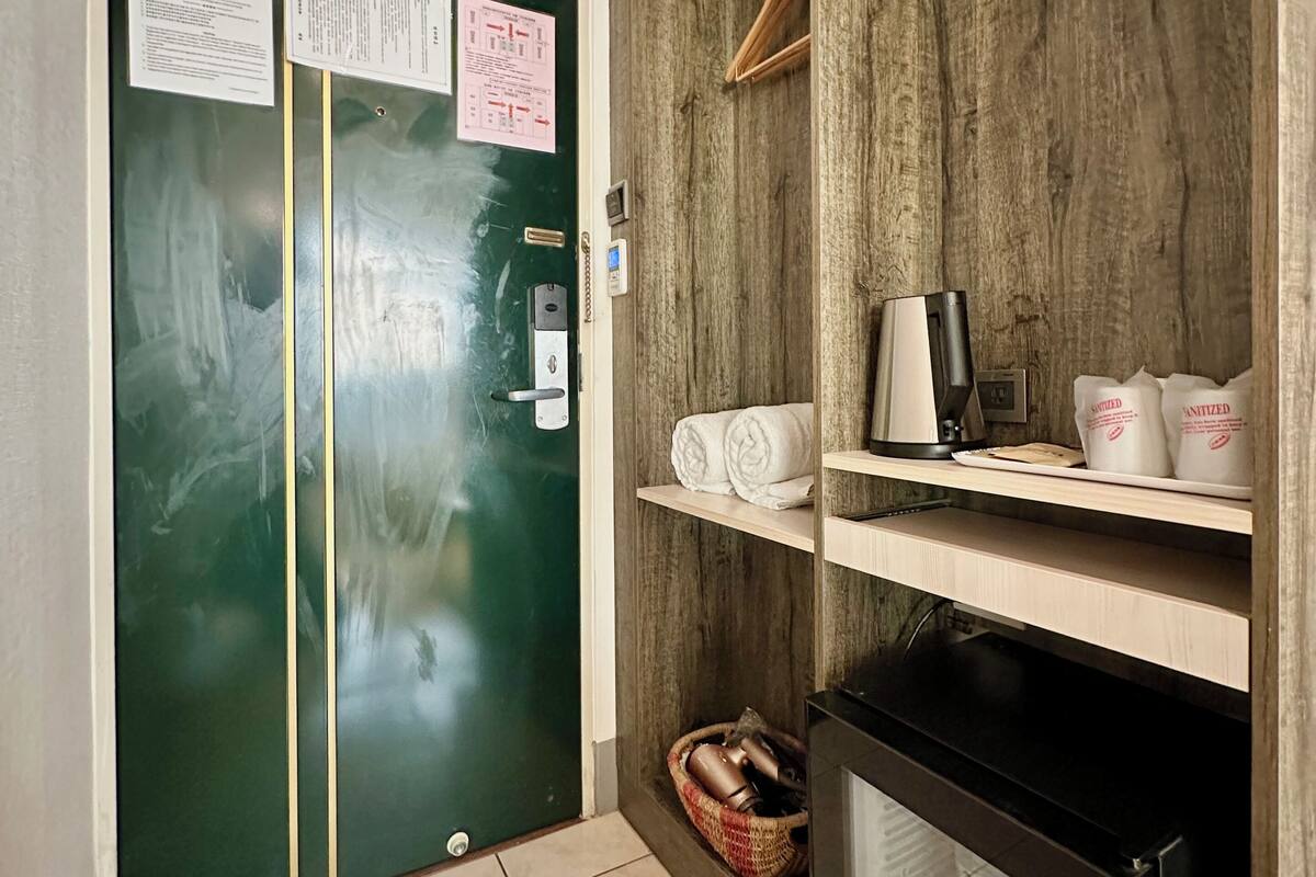 A green door with a notice, a small shelf with towels and a kettle, and a black cabinet with a basket underneath.