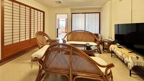Une pièce de style japonais traditionnel, avec un sol recouvert de tatamis, une table basse avec des coussins et un téléviseur posé sur un meuble.
