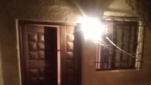 Um quarto com pouca luz, uma porta de madeira e uma janela com grades.