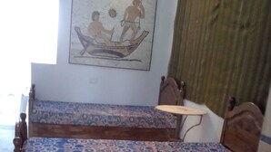 Quarto com duas fileiras de bancos de madeira com almofadas estampadas, uma mesa pequena com um tecido decorativo e um sofá.