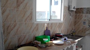 Uma cozinha com azulejos de mármore, uma janela, uma pia, um fogão e diversos utensílios de cozinha na bancada.