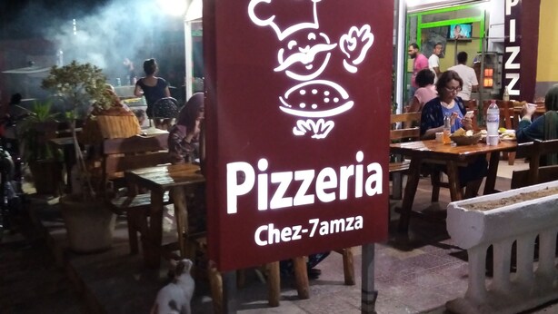 Placa de pizzaria com ilustração de chef e o nome 'Chez-7amza'.