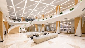 A spacious lobby with a central seating area, multiple levels with staircases, and a modern design with geometric patterns on the ceiling.