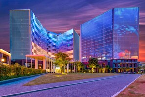 Un hotel moderno con una fachada curva distintiva, un amplio espacio exterior con un sendero pavimentado y una entrada bien iluminada.