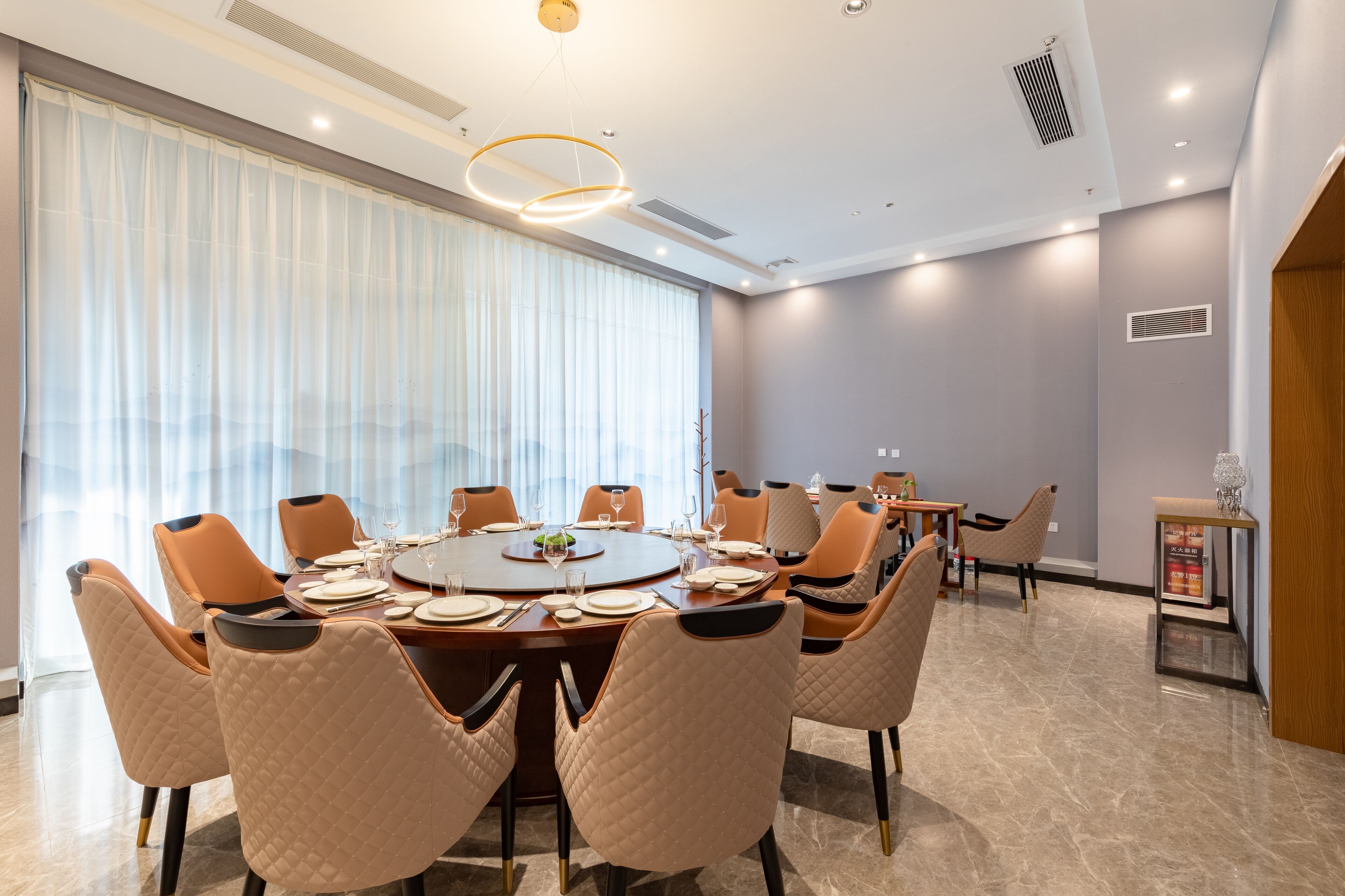 A modern dining area with a round table set for eight, surrounded by cushioned chairs.