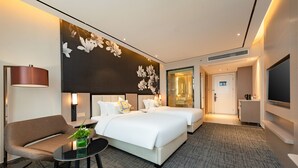 A hotel room with two beds, a sofa, a small table with a plant, and a large wall-mounted TV.