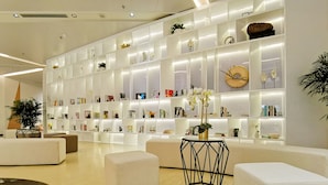 A modern interior with a white bookshelf filled with books and decorative items, a round table with a plant, and a beige sofa.