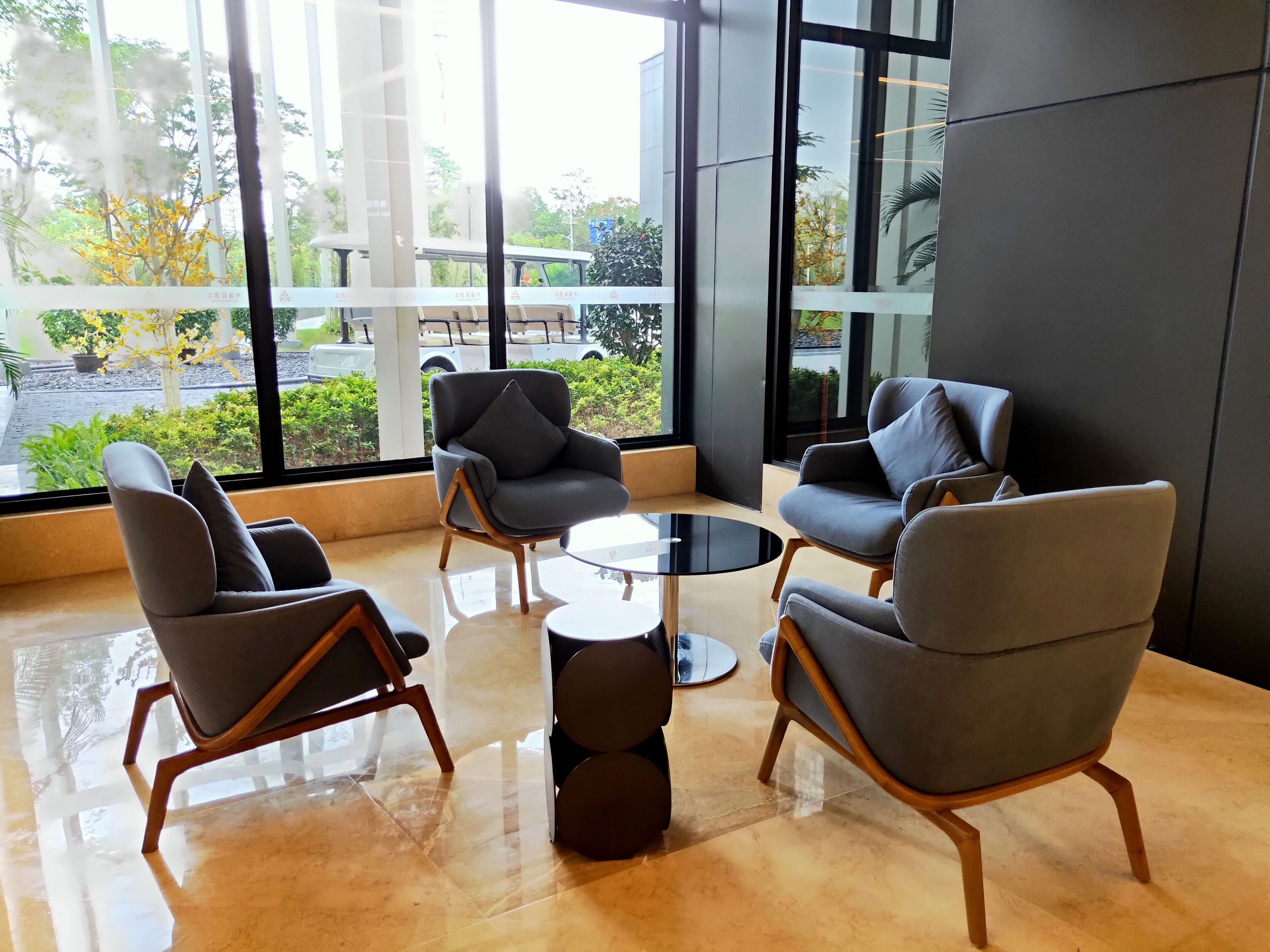 A modern lounge area with a glass wall, contemporary chairs, and a round table.