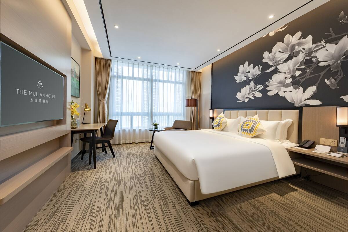 A hotel room with a large bed, a desk, a chair, and a TV on the wall.