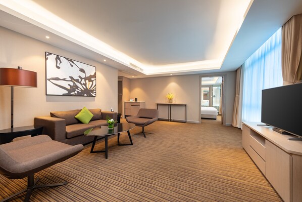 Habitación de hotel con sofá, sillón, mesa de centro, televisor de pantalla plana y un escritorio pequeño.