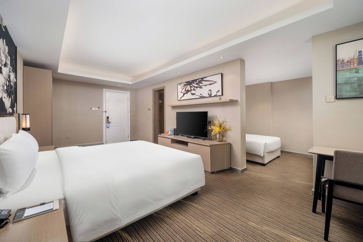 A hotel room with a large bed, a desk with a flat-screen TV, a sofa, and artwork on the walls.