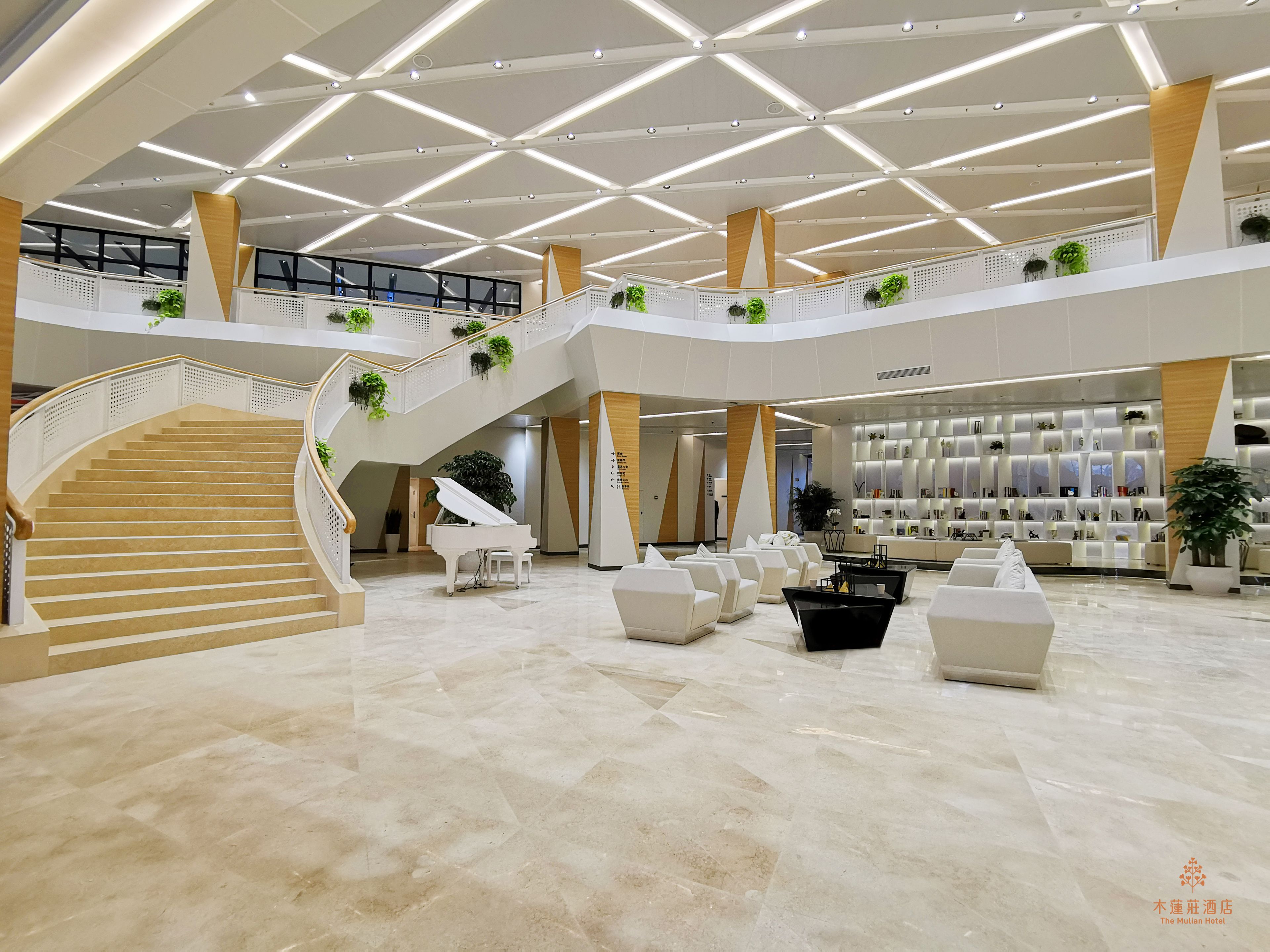 A spacious lobby with a grand piano, multiple seating areas, and a staircase leading to an upper level.