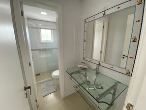 A bathroom with a glass sink, a white toilet, and a shower area. - Apartamento Jurere Internacional (Florianópolis)