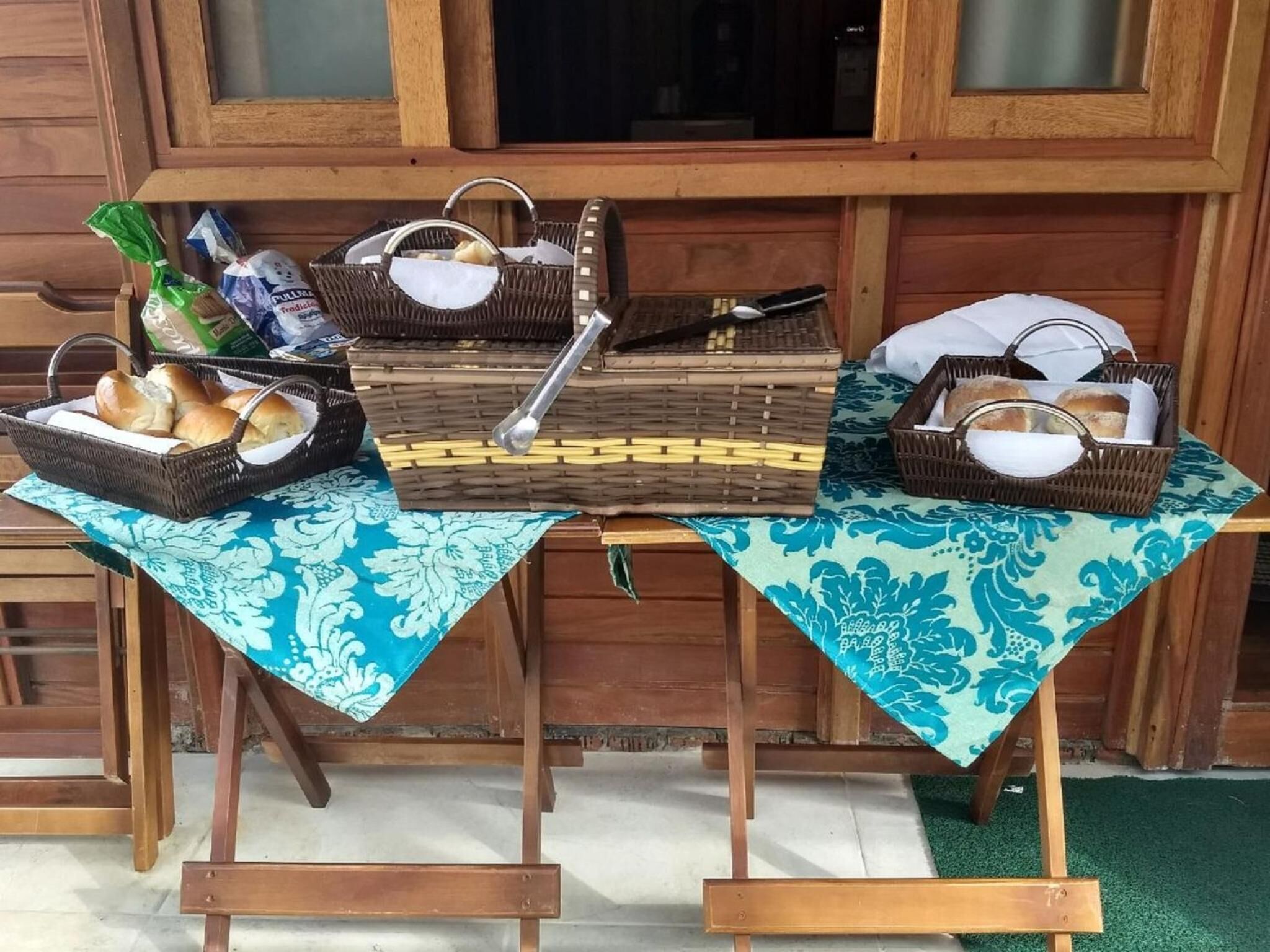 Uma mesa com cestos contendo pão e outros itens, sobre uma toalha de mesa com padrão azul.