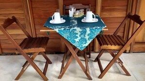 Una mesa de madera con un mantel azul estampado, dos sillas de madera y dos tazas y platillos blancos sobre la mesa.
