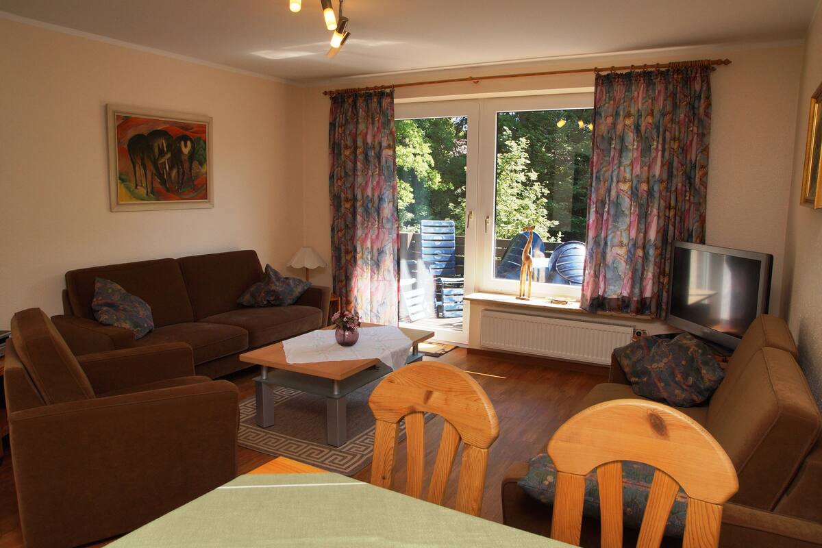 A living room with a sofa, chairs, a coffee table, a TV, and a painting on the wall.