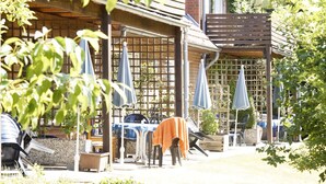 Un área de estar al aire libre con mesas y sillas, protegida por sombrillas y una estructura de pérgola de madera.