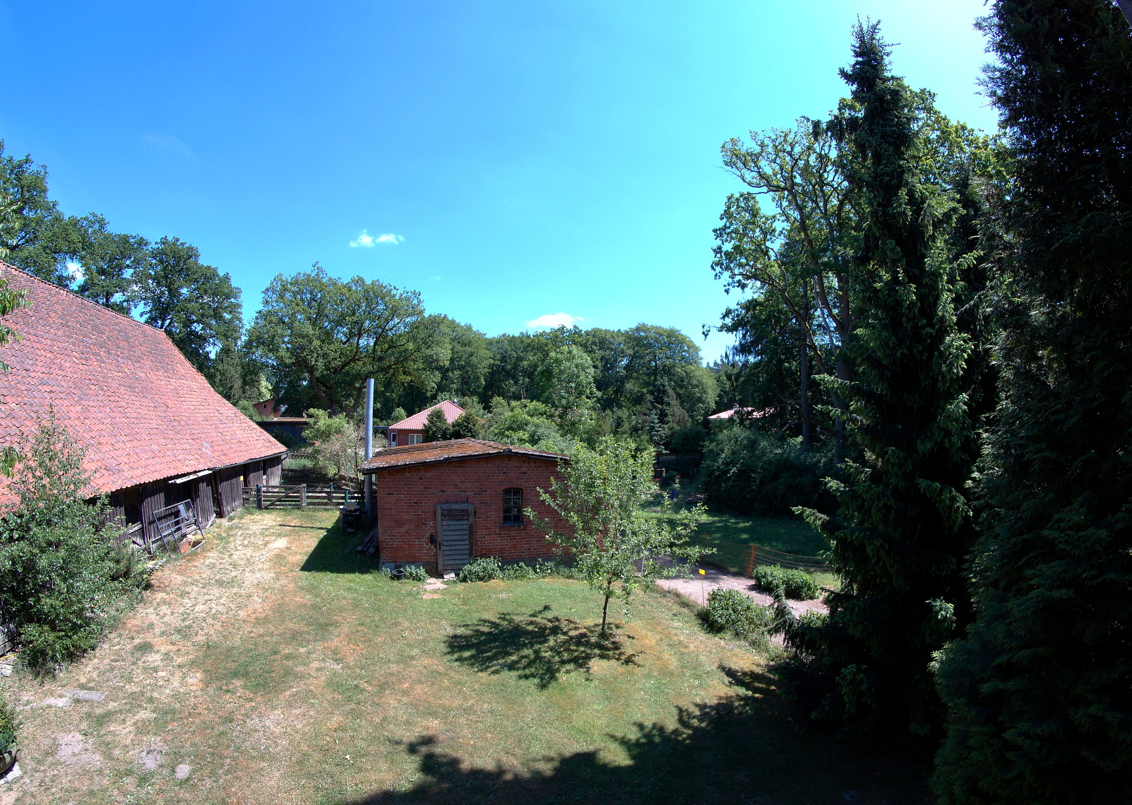 A rural property with a red-roofed barn, a small brick building, and dense surrounding trees.