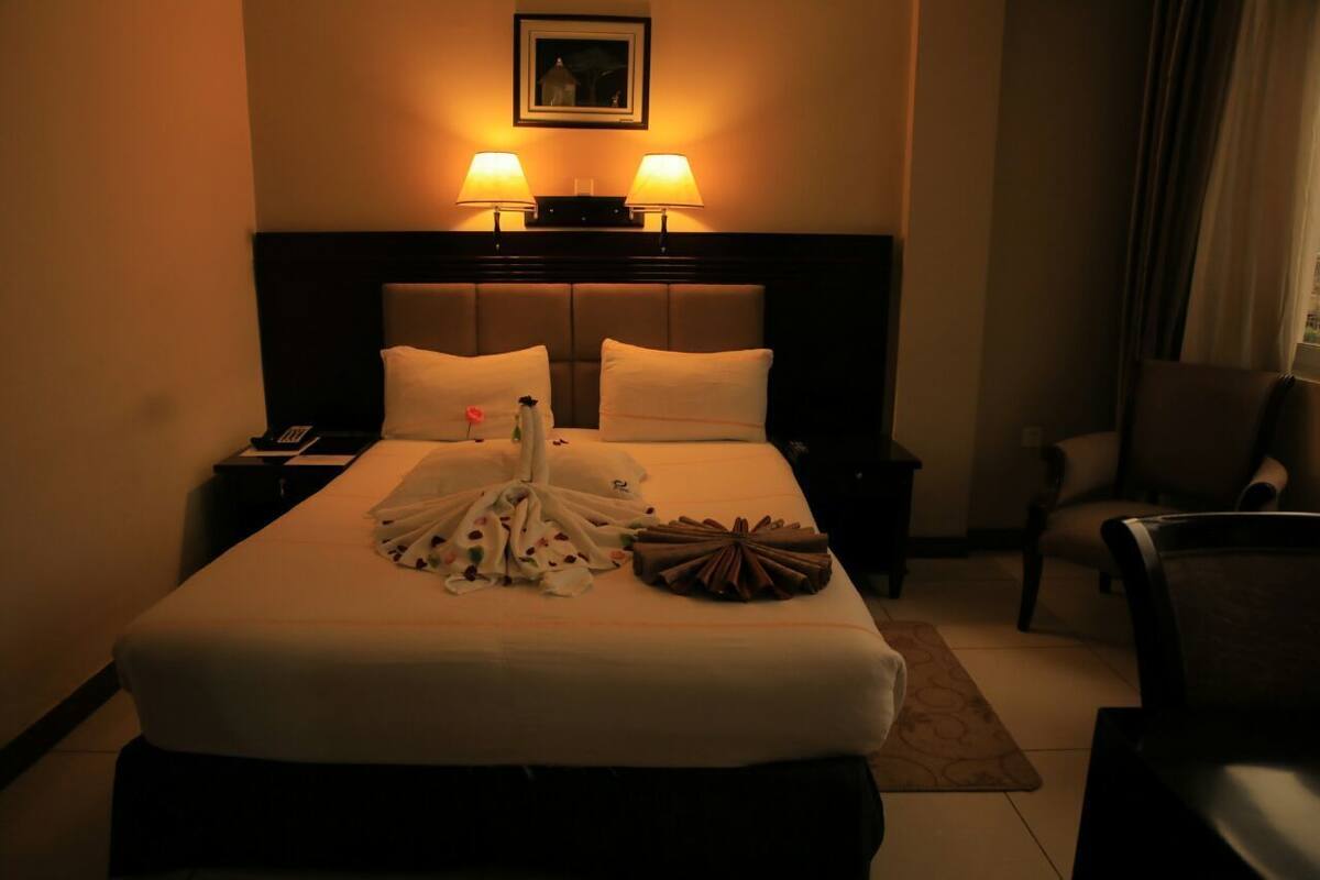 A hotel room with a large bed, two bedside lamps, a nightstand, a chair, and a window with curtains.